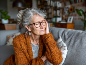 Una donna anziana con i capelli grigi che sembra avere il mal di testa, tenendosi la mano sulla tempia.