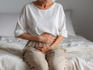 Una persona seduta sul letto si tiene le mani sulla pancia per motivi di incontinenza